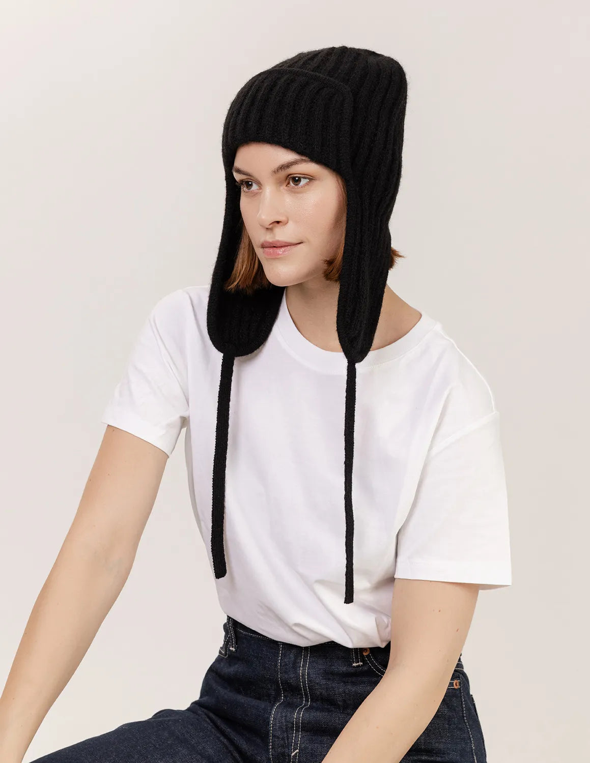Person wearing a black knit hat with long strings on a plain background - Black