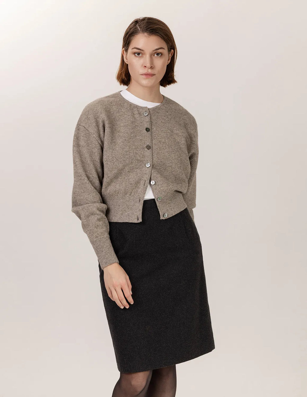 Woman wearing a beige cardigan over a white shirt and dark skirt on a plain background - Natural Grey