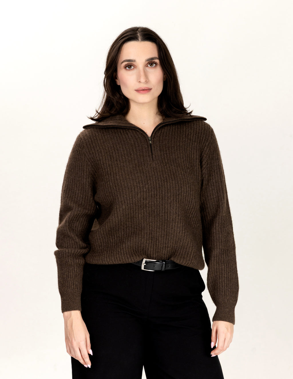 A woman modeling a dark brown ribbed knit half-zip sweater with a stand-up collar, paired with black pants, against a plain white studio background. - Natural Brown