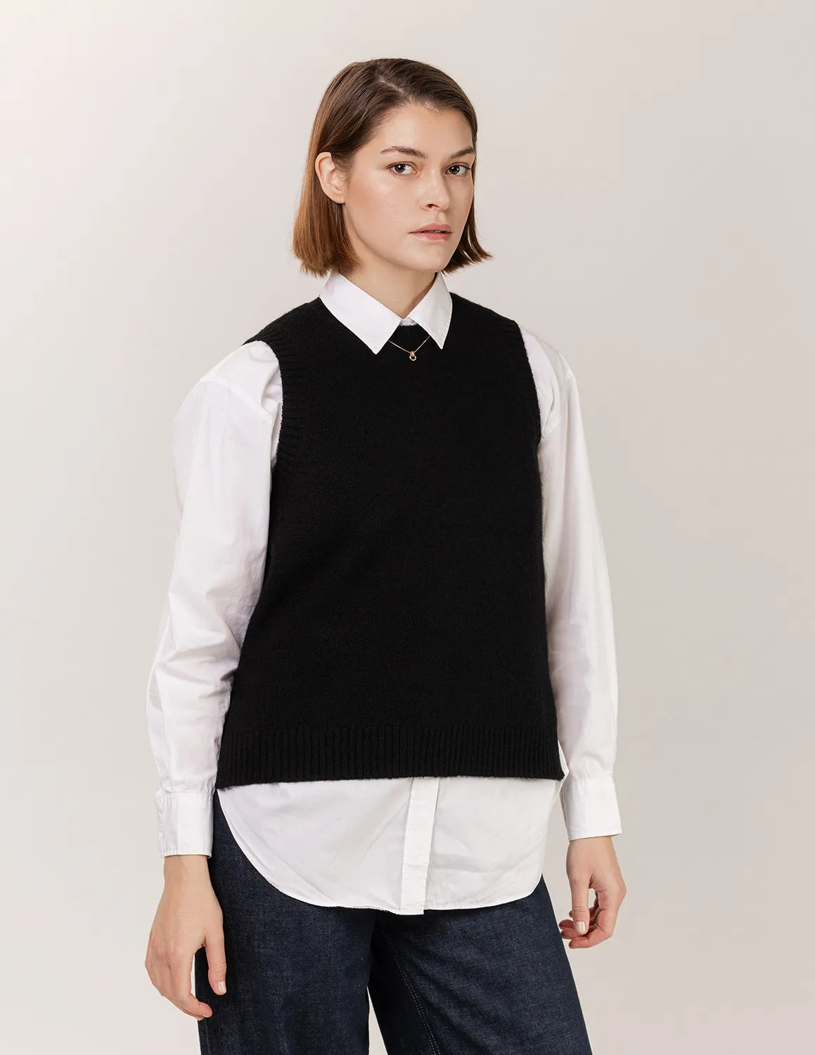 Woman wearing a black vest over a white shirt on a plain background 