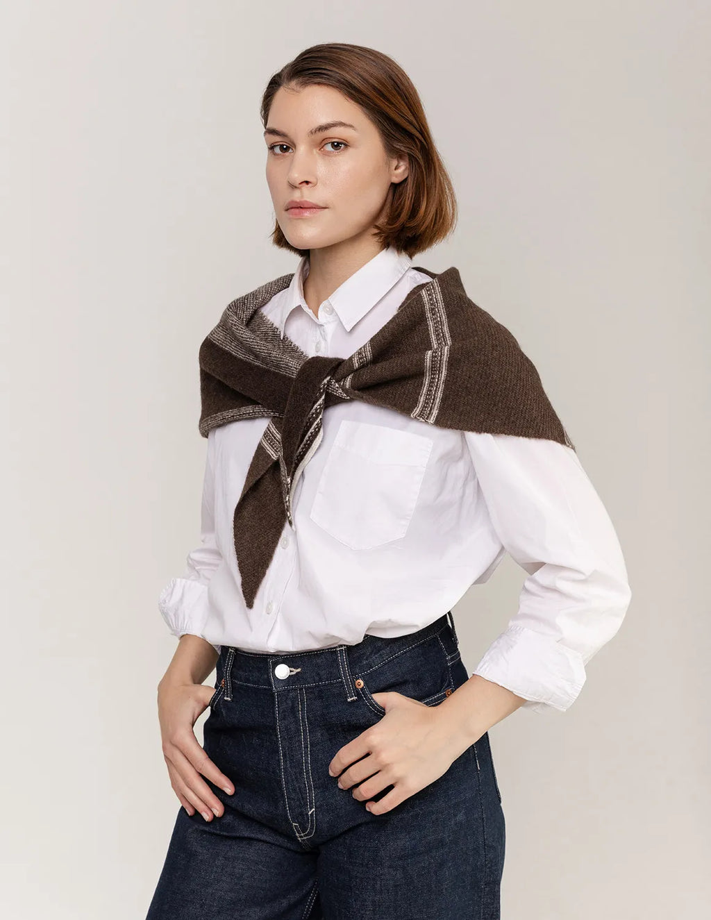 Woman wearing a brown and gray patterned scarf over a white shirt with a plain background