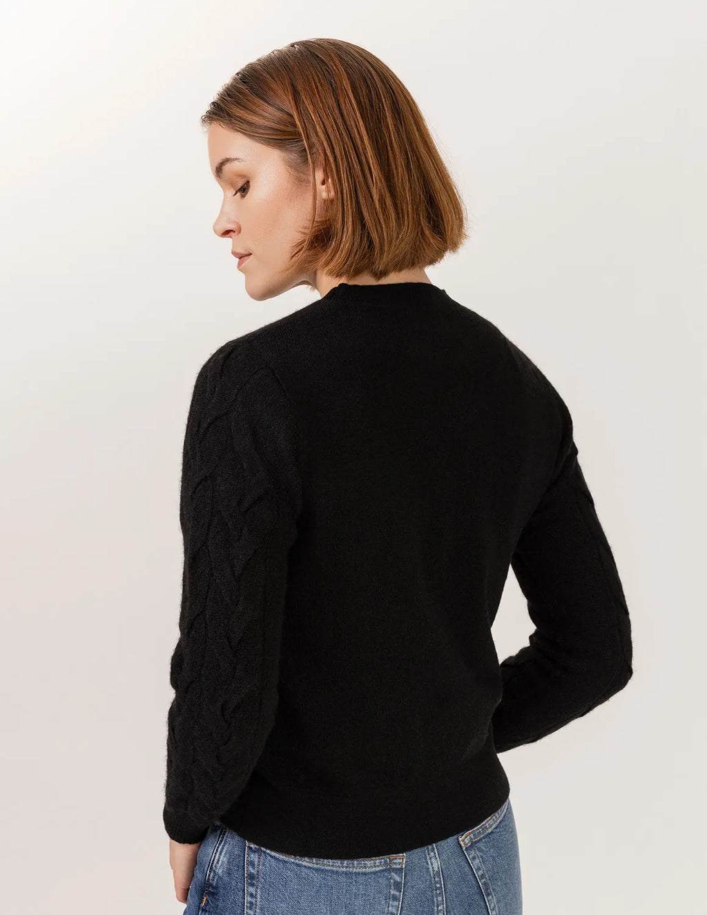 Woman wearing a black sweater and blue jeans on a plain background - Black