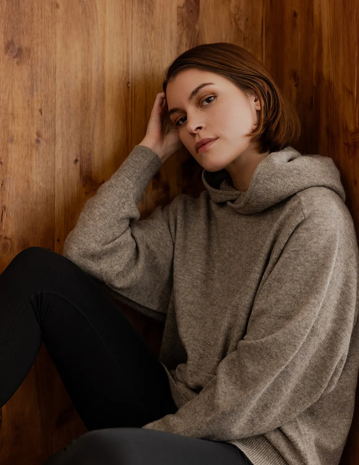 Woman wearing a gray sweater sitting against a wooden wall - Natural Grey