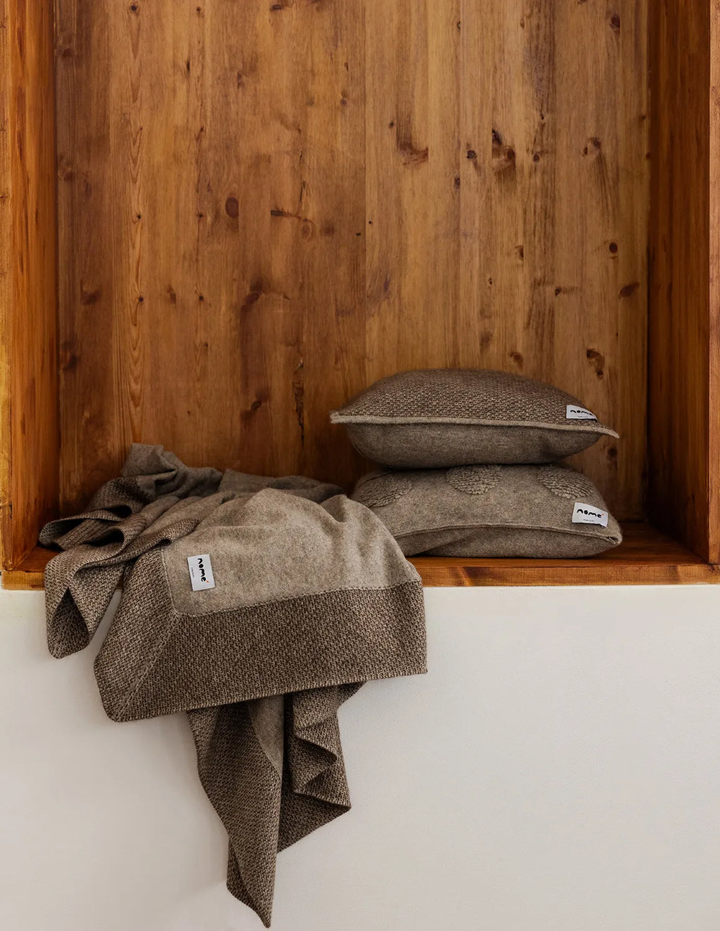 Brown textured pillows and blanket on a wooden shelf against a wooden wall. - Natural Grey