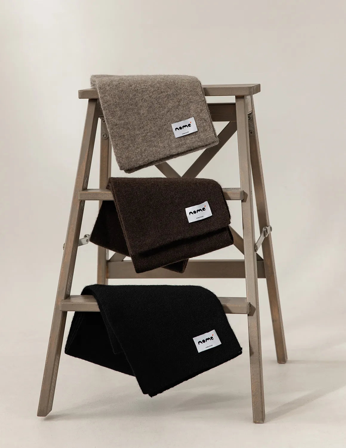Three folded blankets on a wooden ladder against a plain background